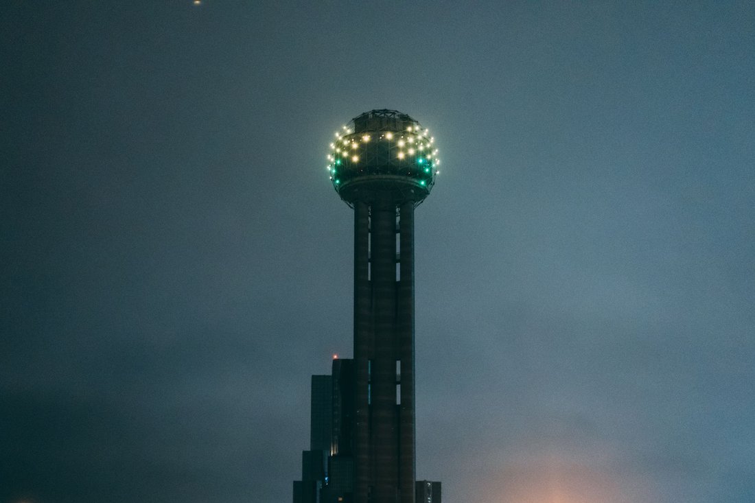 Reunion Tower lit up at night with Dallas downtown skyline reflected in foreground